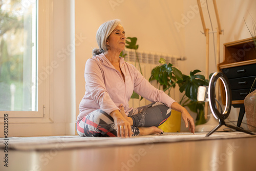 mature woman giving online yoga class from home, pretty senior woman with gray hair doing sports to take care of her health