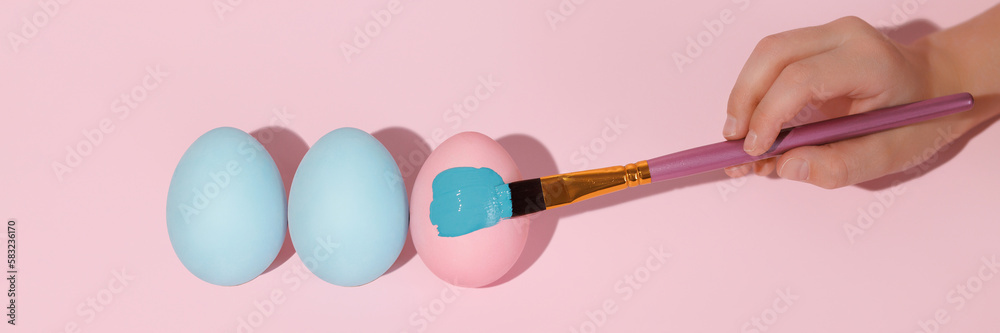 Three colored eggs in a row flat lay. Brush paints a pink Easter egg with blue gouache. Easter colored eggs lie in a row flat lay. Banner for website header design with copy space.