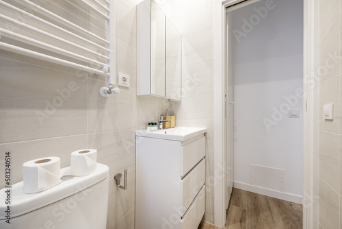 A small bathroom with a white wooden cabinet with drawers  a porcelain sink and a wall cabinet with mirror doors