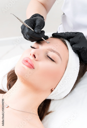 Mechanical facial cleansing with a uno spoon at the beautician clinic. Vertical composition.