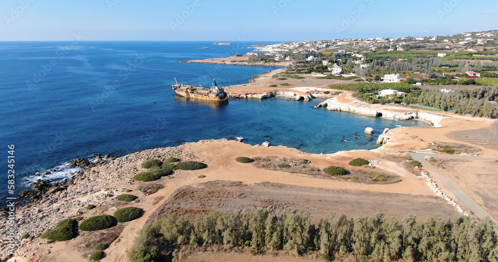 Flying drone over the coastline of the island overlooking an old rusty sunken ship or liner, rocky shoreline with vegetation and rocks and clear sea with light foamy waves in Cyprus.