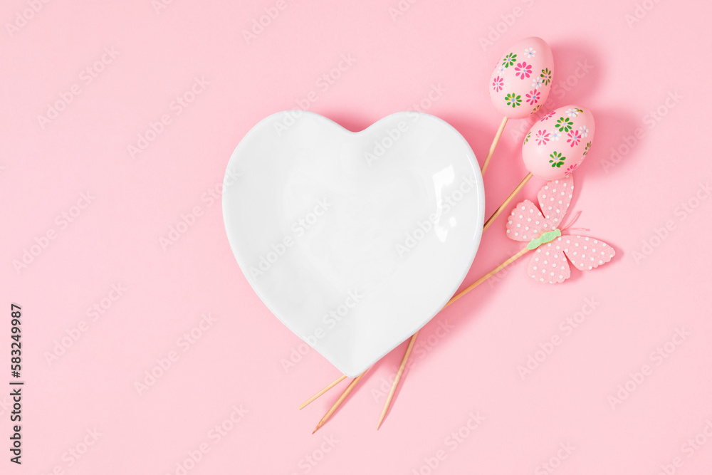 Easter holiday composition. Easter decorations, heart shaped plate on pastel pink background. Easter concept. Flat lay, top view, copy space