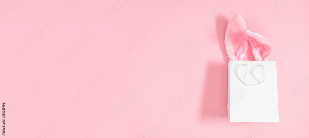 Easter market background, banner. Gift bag with bunny on pink table background. Top view of fluffy easter bunny ears. Concept of online shopping for Easter. Flat lay, top view, copy space