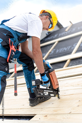 The carpenter nails a timber board using an electric nailer while working on a roof. photo