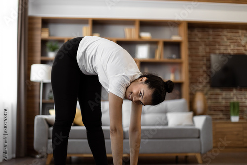 Multiracial active lady dressed in sport clothes warming up before morning exercise at cozy modern apartment. Concept of workout  self-discipline and body care.