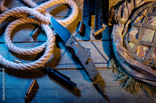 Military composition with a knife and a rope. Rope and sleeves on a military box. Warm yellow light. Knife and flashlight pocket. photo