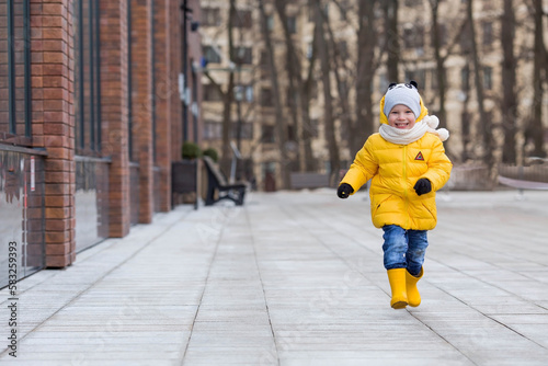 Portrait of a small child 4 years old in yellow rubber boots and a jacket. The kid walks in the park in the spring. Photo of spring and autumn holidays. © Юлия Клюева