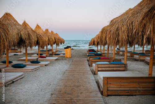 Beds  mattresses and beach pillows placed under the straw umbrellas on the beach.