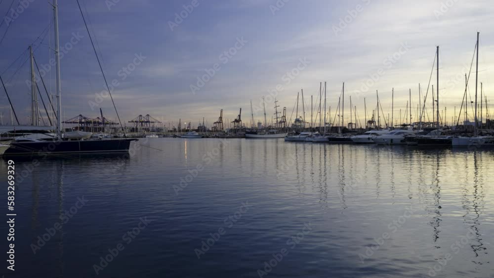 Yachts with reflection in the sea water of the port of Valencia. Port cranes on the horizon. Warm evening in Spain. Yachts with reflection in the sea water of the port of Valencia. Port cranes on the horizon. Warm evening in Spain.