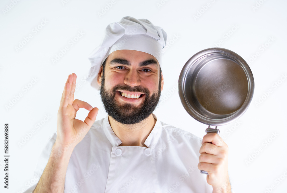 Young male chef showing a stainless saucepan while smiling and looking at camera. Isolated on a white background Young male chef showing a stainless saucepan while smiling and looking at camera. Isolated on a white background