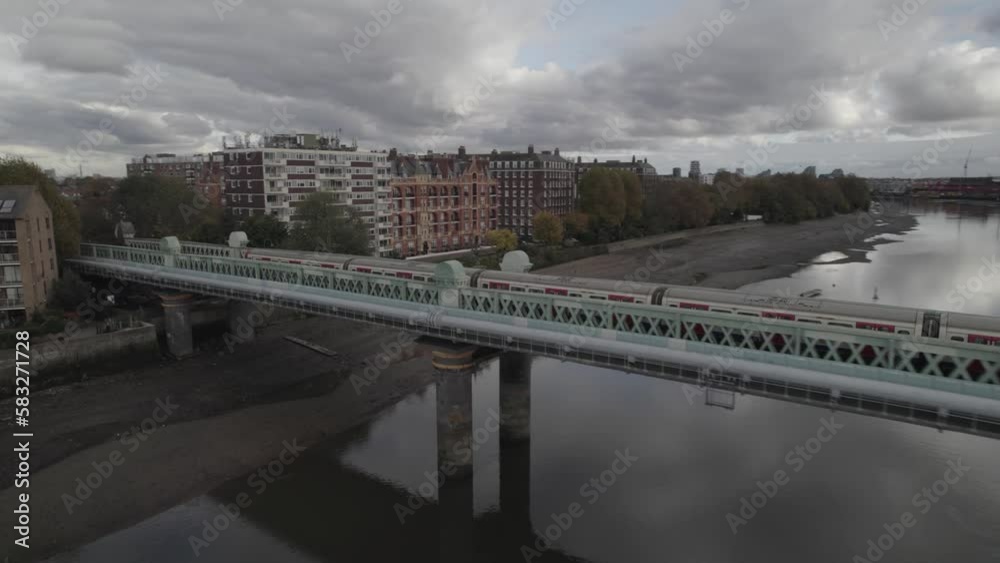 Commuter train passing on bridge over Thames river and heading between buildings in urban neighbourhood. London, UK