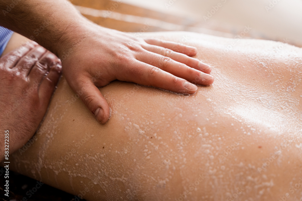 Salt scrub massage on back of girl in spa salon close-up. Masseur making cosmetic scrubbing and peeling procedure for skin rejuvenation. Salt scrub massage on back of girl in spa salon close-up. Masseur making cosmetic scrubbing and peeling procedure for skin rejuvenation.