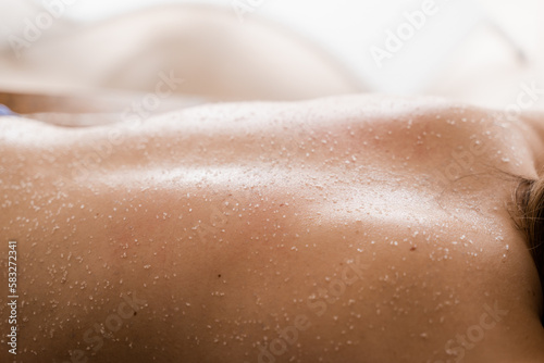 Salt scrub on back of girl in spa salon close-up. Cosmetological procedure of scrubbing, peeling for skin rejuvenation.