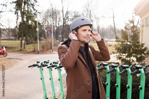 Young man wear helmet and unlocks an electric scooter with his mobile phone. Protective gear in urban city. New way of mobility. Green traffic. Sustainable transportation and climate neutral cities.