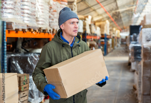 Caucasian man carrying cardboard box while working in warehouse. © JackF