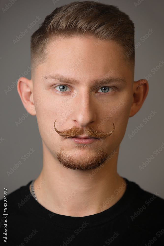 Fototapeta premium Portrait young handsome serious man with curled moustache and beard wears casual black t shirt, looks confidently into camera, has trendy hairstyle, has serious expression, isolated on grey