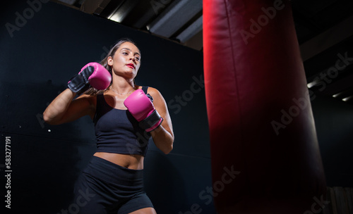 Dark Haired Girl Boxing a Punching Bag in a Moody Setting © Dewald