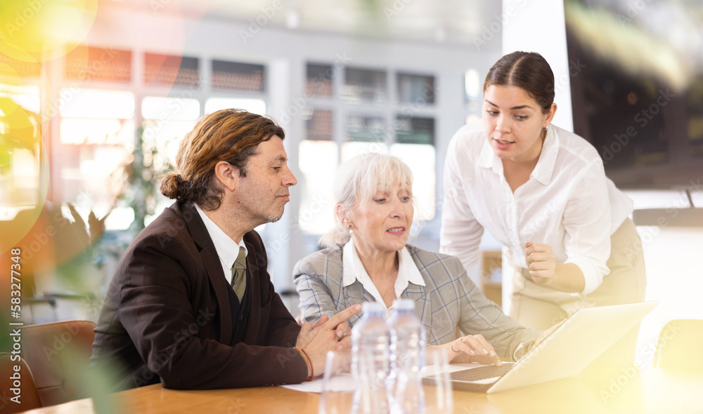 Adult man, elderly woman and young woman having discussion at table in office