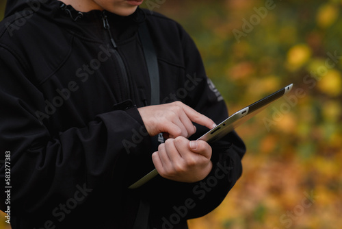 horizontal photo close-up boy with tablet near school with online learning book, slide your finger across the screen, tablet in child's hands, schoolgirl, on beautiful yellow-green background