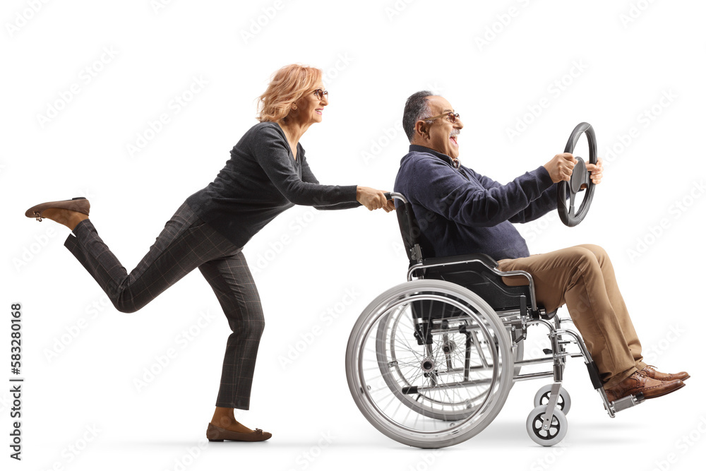 Woman pushing a man in a wheelchair sitting and holding a steering wheel Woman pushing a man in a wheelchair sitting and holding a steering wheel