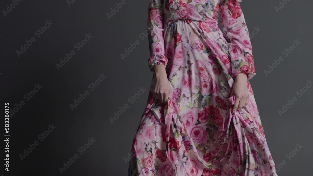 A girl in a long colored dress with flowers on which a strong wind blows, covering the girl's face and creating the effect of movement.