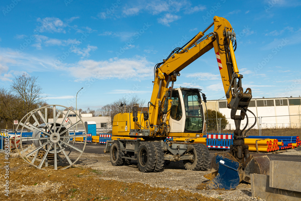 Yellow excavator at a construction site next to an empty cable drum. Blue sky with light clouds.