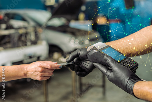 Close-up of auto mechanic worker and hands of female customer paying by credit card during periodic car condition check. photo