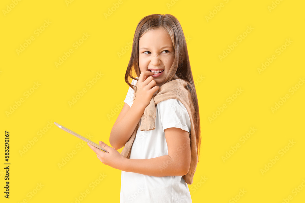 Little girl with tablet computer biting nails on yellow background Little girl with tablet computer biting nails on yellow background