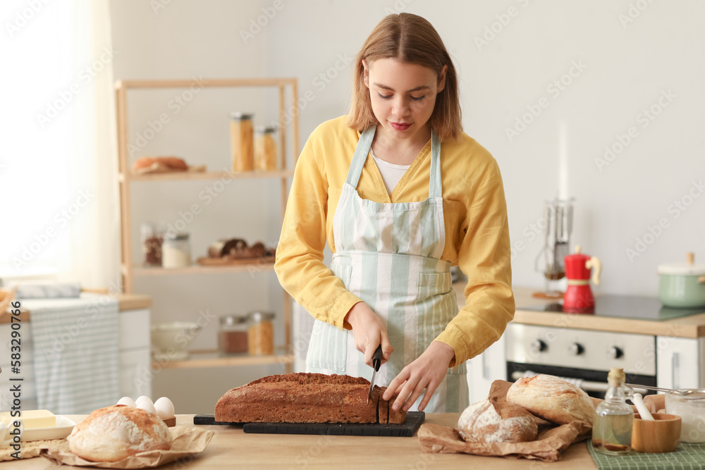 Female baker cutting rye bread at table in kitchen