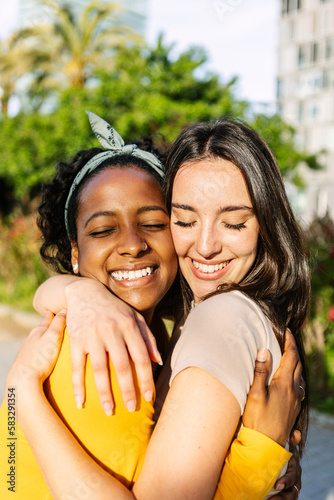 Canvas Print Vertical portrait of candid happy multiracial best women friends embracing outdoors