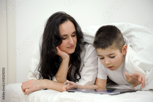boy, And his mother is working on a laptop computer, The little boy put the tablet in his hand and turned to his busy mother intently, wanting his mother to pay attention to him. High quality photo