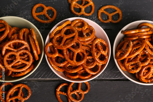 Bowls with tasty pretzels on dark color background, closeup