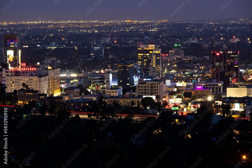 Looking down on Hollywood as night falls on the city and the lights of Los Angeles begin to twinkle, with even the Port of Los Angeles in the distance