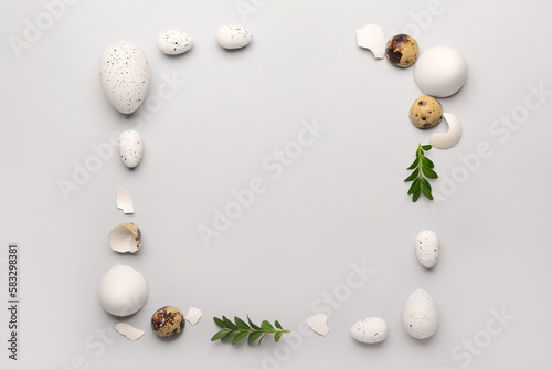 Frame made of Easter eggs and plant leaves on grey background