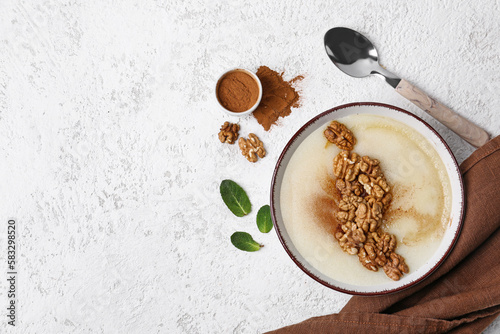 Bowl of tasty semolina porridge with nuts and cinnamon on light grunge background