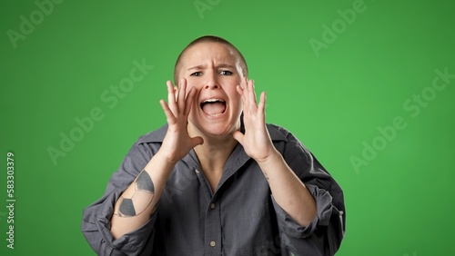 Portrait of gender fluid non binary young woman 20s angry upset shout calling inviting with hands at mouth say HEY YOU isolated on green screen background.