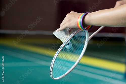 Badminton player wears rainbow wristbands and holding racket and white shuttlecock in front of the net before serving it to player in another side of the court, concept for LGBT people activities. © Sophon_Nawit