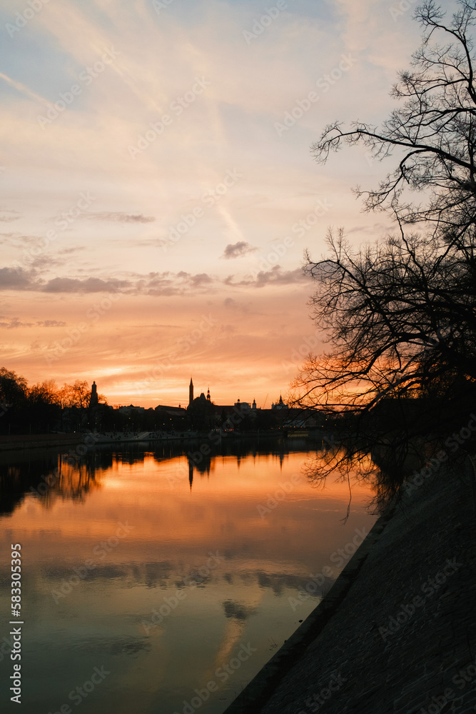 Sunset over the river in Wrocław, Poland. Dark trees, dramatic clouds on the sky.