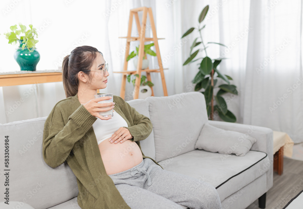 pregnant asian people sitting on sofa, she drinking fresh milk and use her hand touch on her abdomen, she feeling love and care her daughter, pregnancy health care promotion pregnant asian people sitting on sofa, she drinking fresh milk and use her hand touch on her abdomen, she feeling love and care her daughter, pregnancy health care promotion