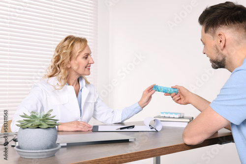 Doctor holding box of pills and consulting patient at table in clinic