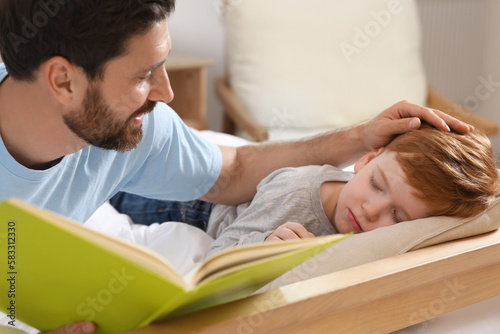Father reading book with his child on bed at home, closeup