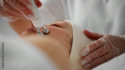 A cosmetologist in gloves conducts aqua peeling of the skin of a young woman's face in a cosmetology clinic Professional hardware moisturizing and rejuvenation procedures modern people