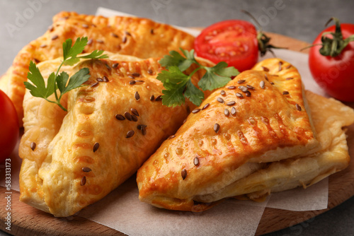 Fresh delicious puff pastry with cheese, tomatoes and parsley on wooden board, closeup