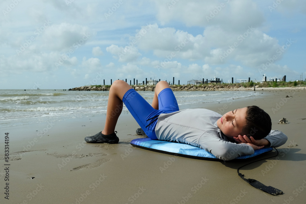 Young preteen boy laying on boogey board outside on the beach