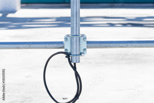 Nuts clamp aluminum cable duct electric wire small like cross. Fixing screws electric pole for help pull support from falling in wind. Blurred blue concrete wall background. Concept safety fastening.