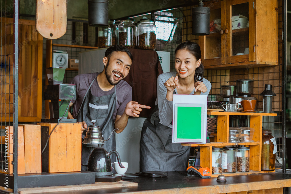 a couple of barista pointing on the digital tablet with green screen while standing inside the bar desk