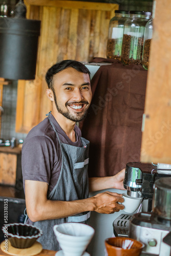 asian male barista in apron standing with smile while operating the coffee machine at the coffee shop