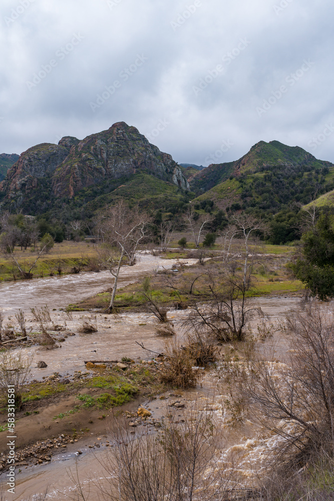 Malibu Creek State Park muddy after a large rainfall in southern California. Streams overflowing, lush green grass, large oak trees, clouds, dam rushing, water flowing. Malibu Creek State Park muddy after a large rainfall in southern California. Streams overflowing, lush green grass, large oak trees, clouds, dam rushing, water flowing.