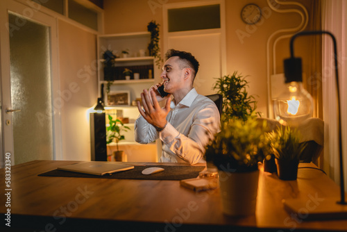 A young man is working late or studying at his home office while drinking coffee and using his mobile phone	