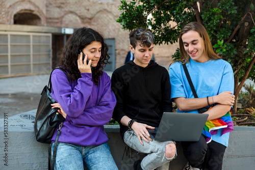 Young diverse people with lgbt rainbow flag using laptop and mobile outdoors.
